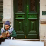 Elderly man sits reading outside a green doorway in Buenos Aires, Argentina, capturing a moment of urban tranquility.