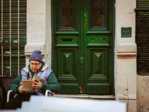 Elderly man sits reading outside a green doorway in Buenos Aires, Argentina, capturing a moment of urban tranquility.