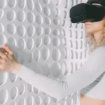 Woman explores a white textured wall using virtual reality headset, capturing advanced tech and tactile perception.