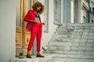 Stylish young woman in red suit standing by an ornate wooden door in an urban setting.