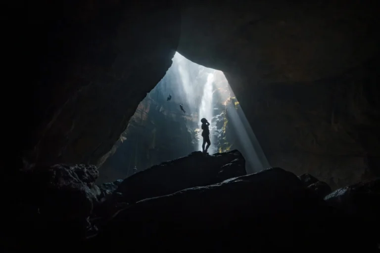 Silhouette of a person in a cave with dramatic light beams from above.