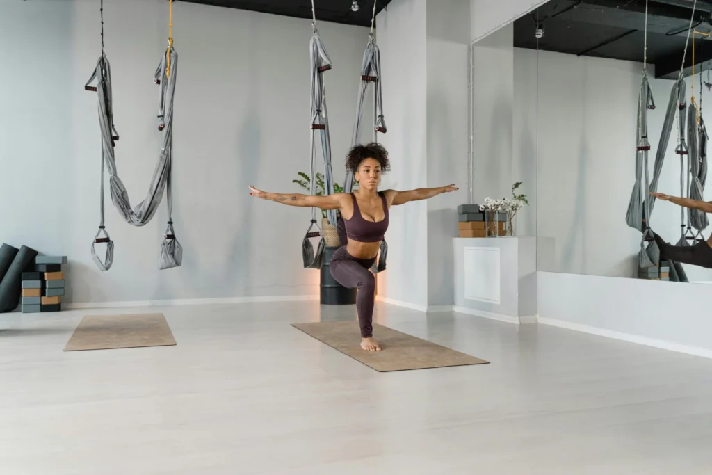 A woman in activewear practicing yoga indoors, demonstrating balance and flexibility with aerial equipment.