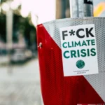 Sticker advocating against climate crisis on a red post in a city street, emphasizing climate action.