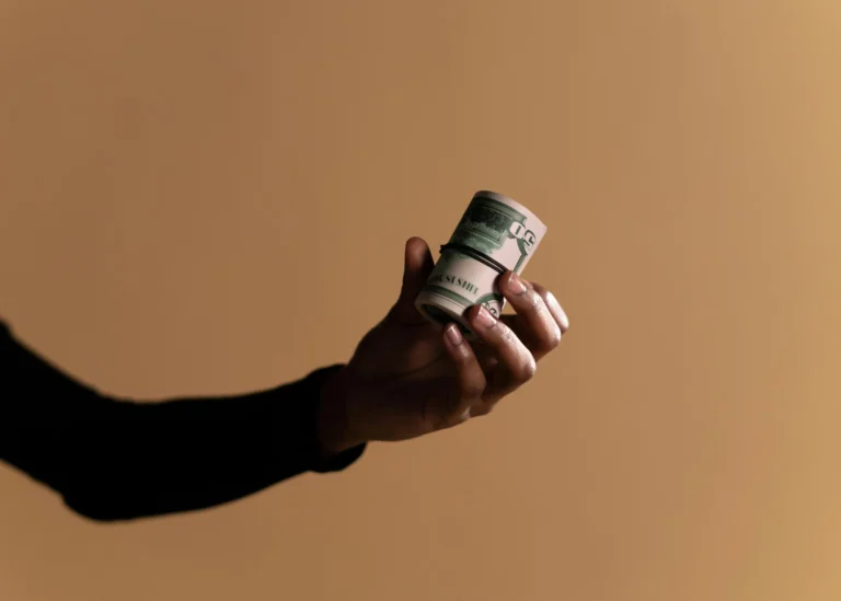 A close-up image showing a hand holding a roll of money against a beige background, ideal for finance themes.