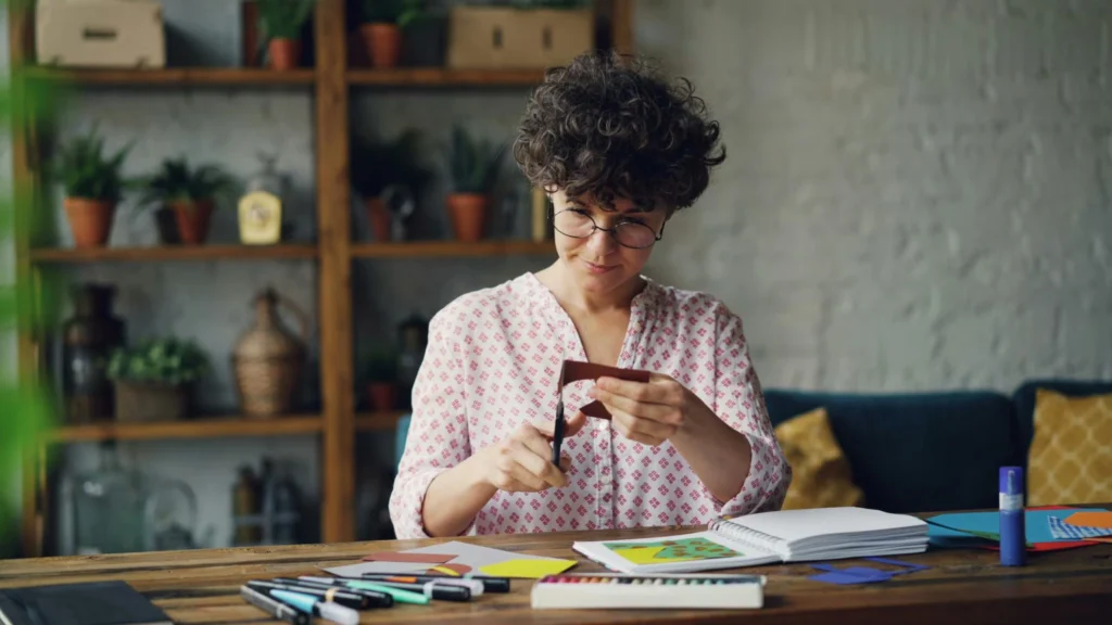 Woman engaged in crafting activities with paper and scissors in a cozy indoor setup.