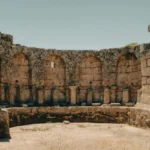 Ancient stone ruins feature historic arches and rugged landscape under clear sky.