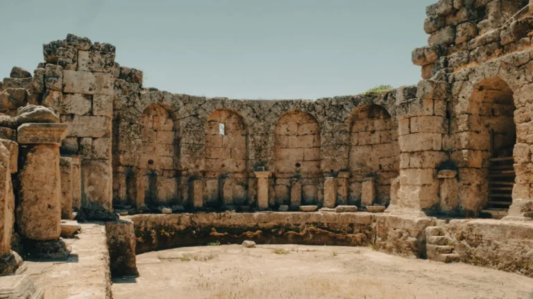 Ancient stone ruins feature historic arches and rugged landscape under clear sky.