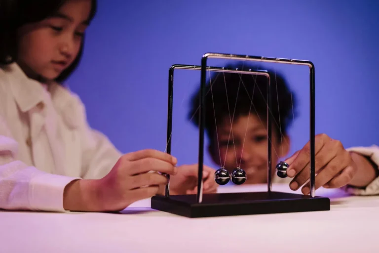 Two diverse children exploring physics concepts with a Newton's Cradle in a studio.