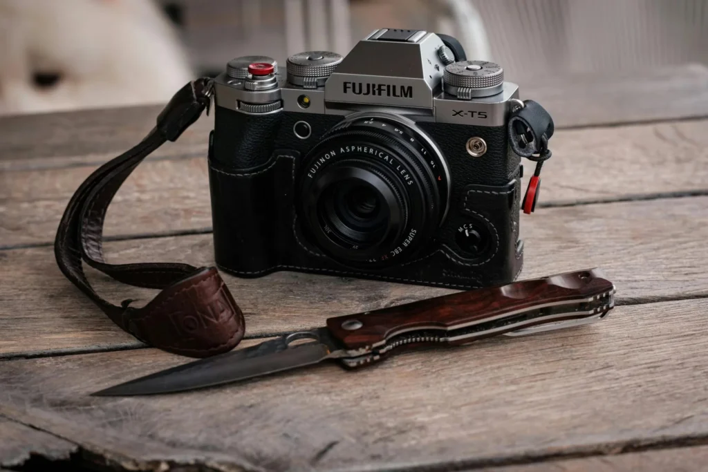 Fujifilm X-T5 camera with lens and folding knife on a rustic wooden table.