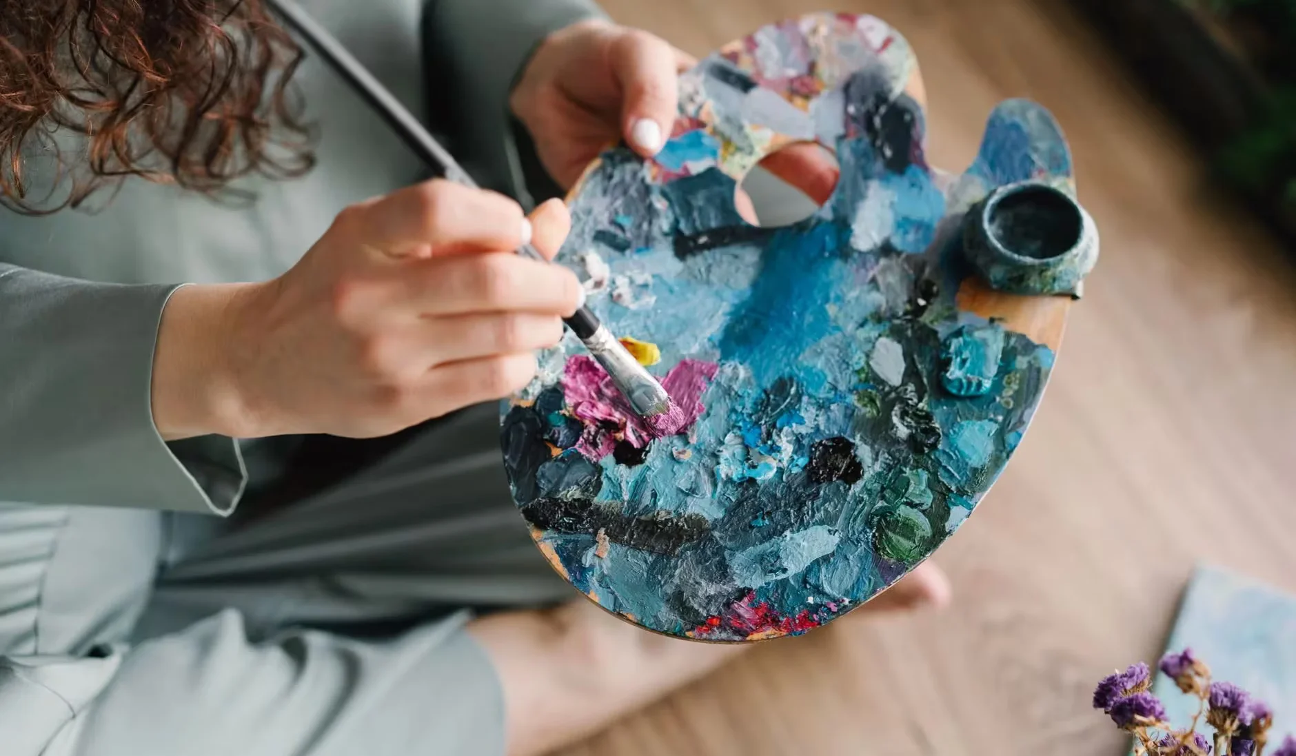 Close-up of hands painting on a colorful palette, showcasing creativity and artistry.
