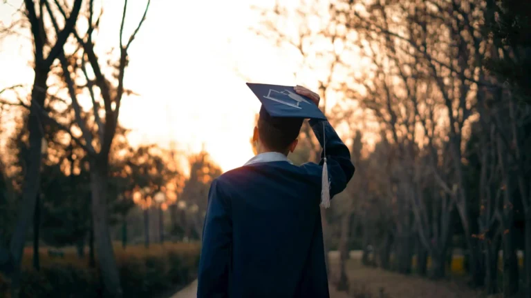 A graduate in a cap and gown celebrates outdoors during sunset.