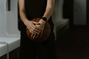 A close-up shot of a basketball player holding a ball in a dimly lit indoor space.
