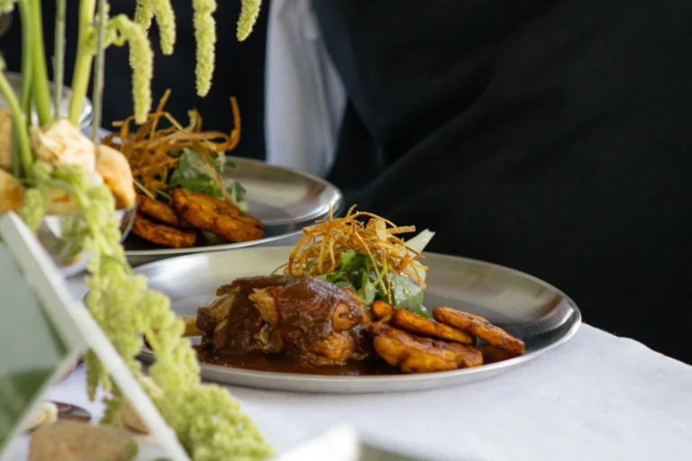 A delicious gourmet dish with meat, fried plantains, and greens, served on a silver platter.