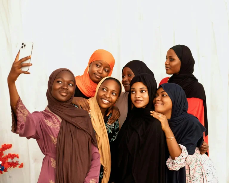 A group of young women in colorful clothing happily taking a selfie indoors.