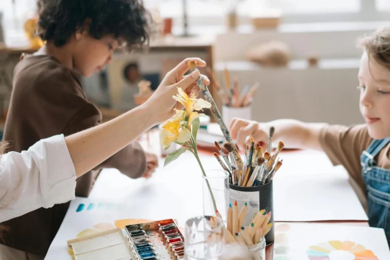 Children painting and drawing together in an art workshop, holding paintbrush and using colors.