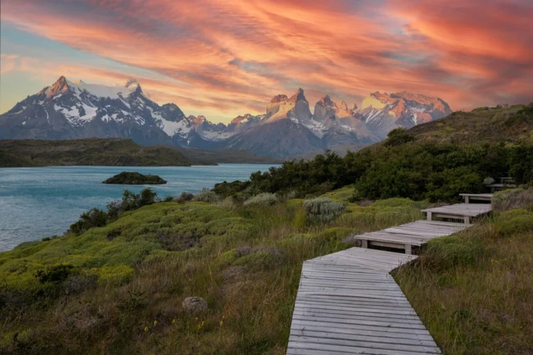 Wooden boardwalk leading to Torres del Paine mountains under a vibrant sunset sky in Chile.