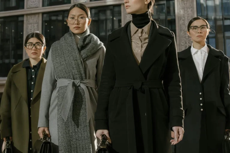 A group of fashionable women in coats standing confidently in an urban environment.