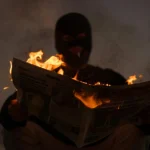 A masked person holds a burning newspaper in dramatic low light, evoking mystery.