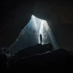 Silhouette of a person in a cave with dramatic light beams from above.