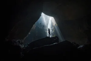 Silhouette of a person in a cave with dramatic light beams from above.