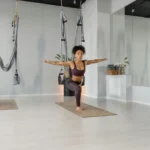 A woman in activewear practicing yoga indoors, demonstrating balance and flexibility with aerial equipment.