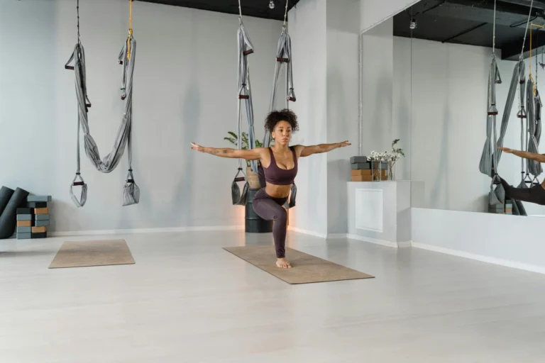 A woman in activewear practicing yoga indoors, demonstrating balance and flexibility with aerial equipment.