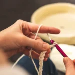 A focused shot of hands crocheting with a pink hook and white yarn, showcasing the art of crafting.