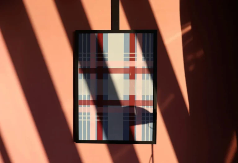 Abstract plaid artwork framed on a pink wall with dynamic shadows in natural light.