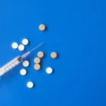 Top view flat lay composition of set of medical syringe and various pills placed on blue background