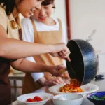 Two women preparing a pasta dish, showcasing teamwork and cooking skills in a cozy kitchen setting.