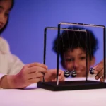 Two diverse children exploring physics concepts with a Newton's Cradle in a studio.
