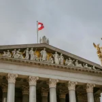 Front view of Austrian Parliament Building with Athena statue and national flag.