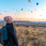 Woman watching hot air balloons in Cappadocia at sunrise, a popular travel destination.