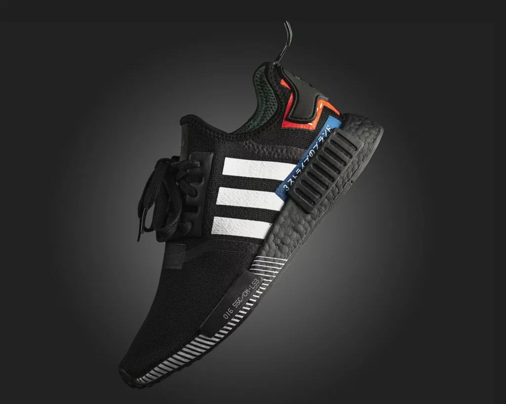 Close-up photo of a black Adidas NMD sneaker with detailed textures on a dark background.