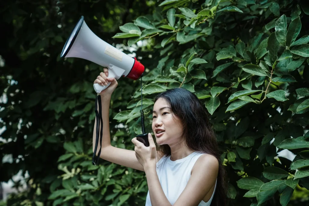 Confident young woman with megaphone at an outdoor rally, advocating for change.