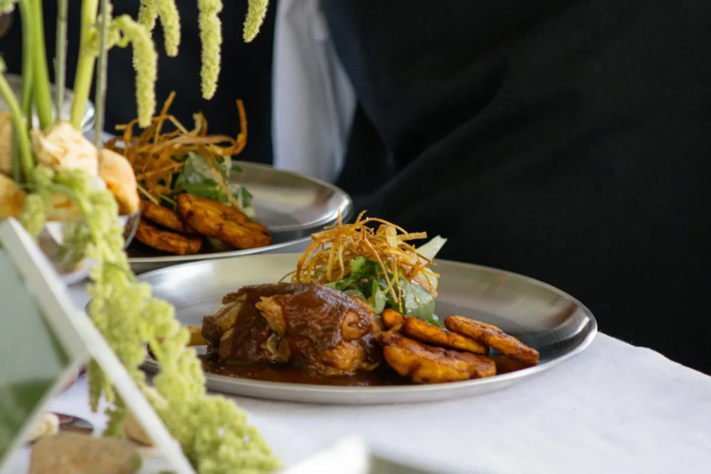 A delicious gourmet dish with meat, fried plantains, and greens, served on a silver platter.