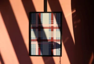 Abstract plaid artwork framed on a pink wall with dynamic shadows in natural light.