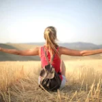 Woman enjoying the open air and freedom while sitting in a hay field during sunset.
