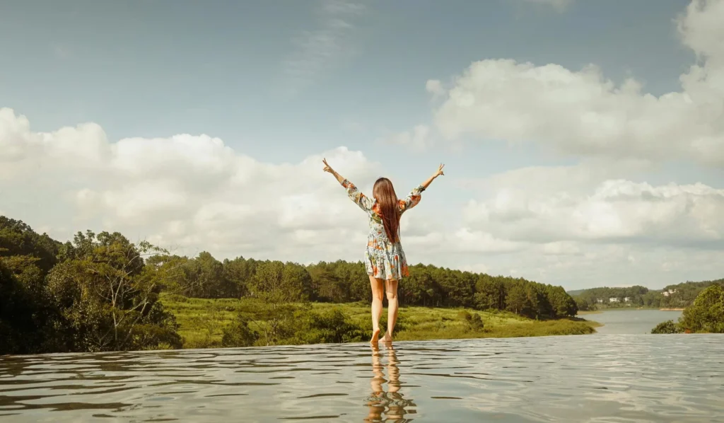 A woman stands with arms raised, enjoying a serene lakeside view in Dalat, Vietnam.