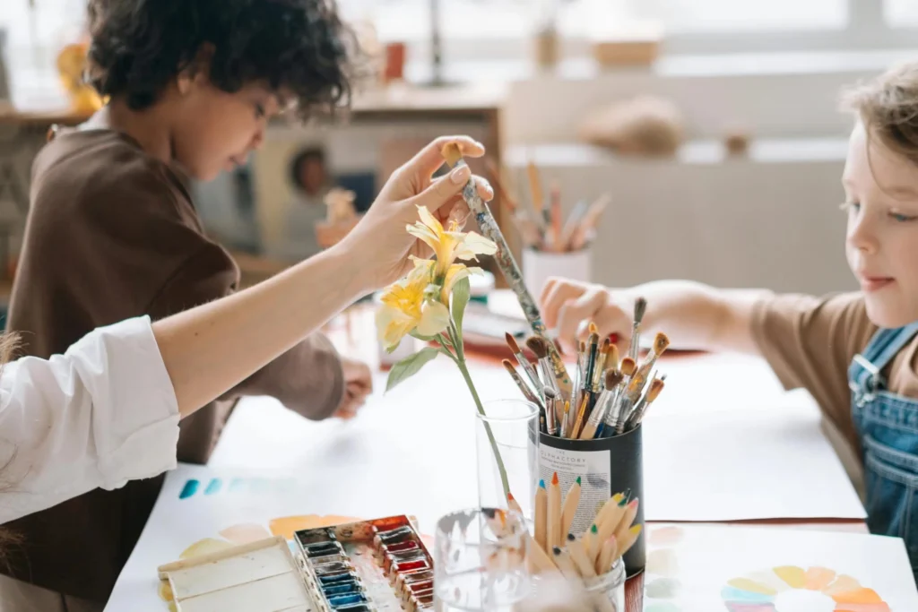 Children painting and drawing together in an art workshop, holding paintbrush and using colors.