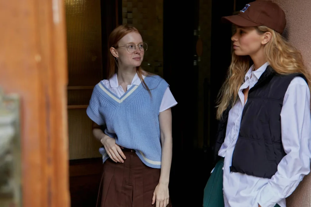Two stylish women in casual wear share a candid outdoor moment, showcasing modern street fashion.