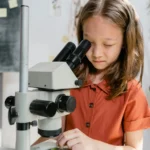 A curious girl examining a sample using a microscope in a classroom setting, focused on learning science.