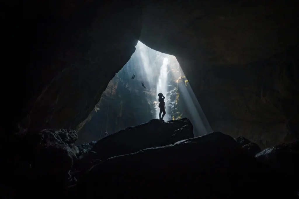 Silhouette of a person in a cave with dramatic light beams from above.