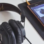 A close-up of headphones and a smartphone playing music on a desk.