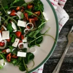 A vibrant and colorful spinach salad with feta cheese and tomatoes on a rustic table.