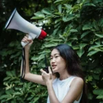 Confident young woman with megaphone at an outdoor rally, advocating for change.