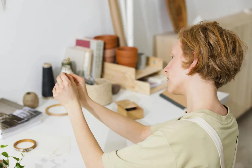 Caucasian woman crafting in a minimalist workspace with sewing supplies and plants.