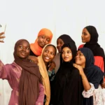 A group of young women in colorful clothing happily taking a selfie indoors.