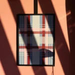 Abstract plaid artwork framed on a pink wall with dynamic shadows in natural light.