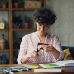 Woman engaged in crafting activities with paper and scissors in a cozy indoor setup.
